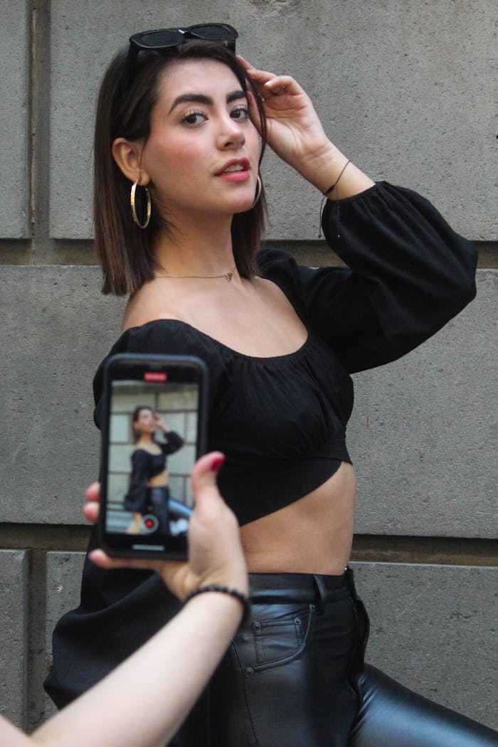 Fashionable young woman poses outdoors as a friend takes her picture with a smartphone.