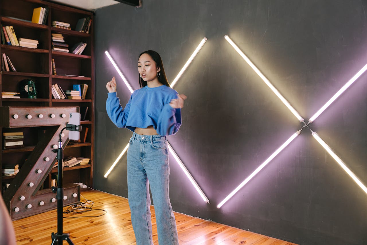Asian woman filming video content in a trendy room with neon lighting and bookshelves.